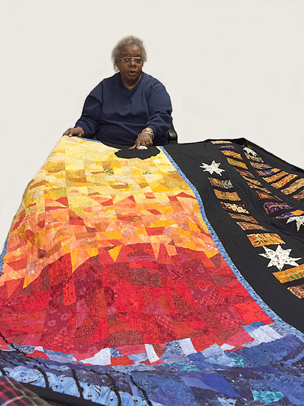 Naomi Henry holding her Jazz Divas quilt, African American quilting guild, 2005; Sisters in Stitches: Joined by the Cloth; Grove Hall, Massachusetts; Cotton and synthetic fabric; 45 x 60 inches; Photography by Maggie Holtzberg